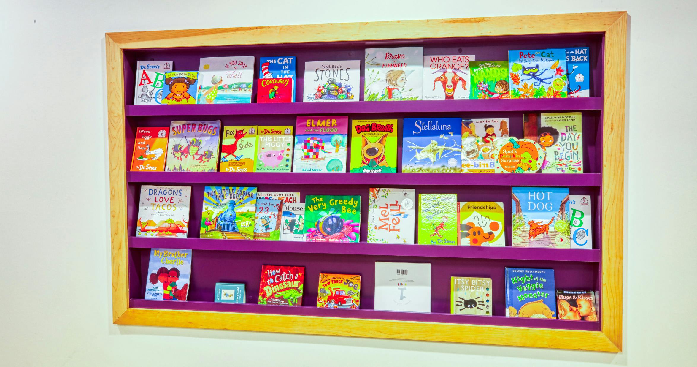 Children's books displayed on purple shelves in a wooden frame