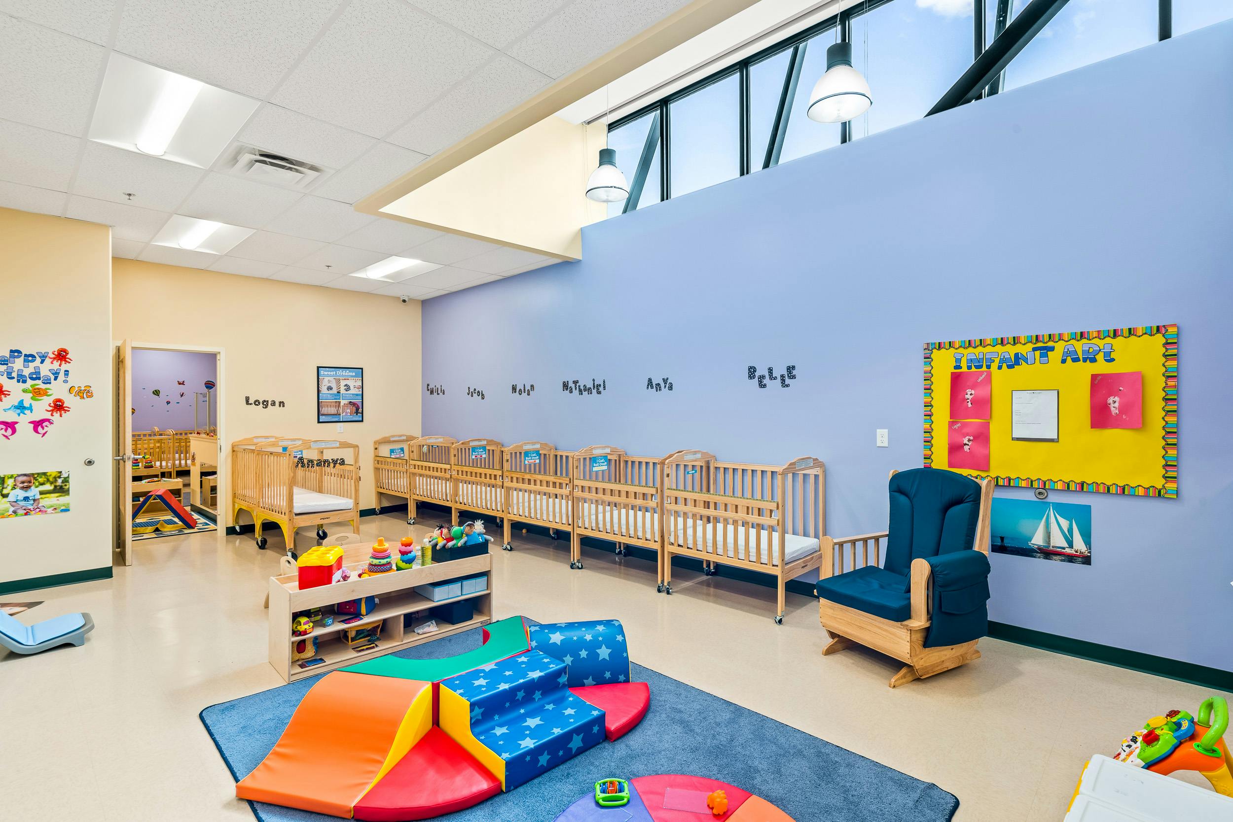 Nursery room with multiple cribs, a blue rocking chair, and soft play equipment