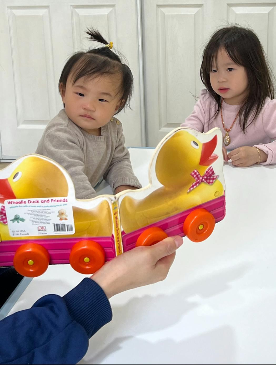 Two children looking at a toy duck train held by a person
