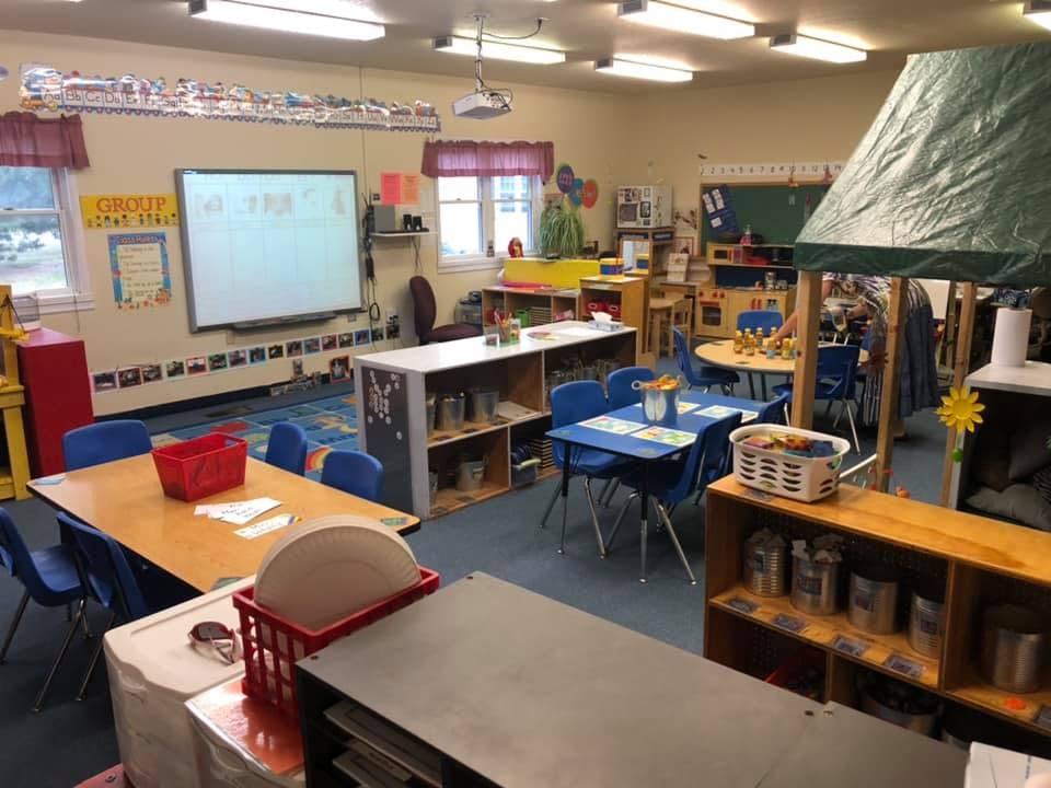 Classroom with small tables and chairs, shelves, and a whiteboard