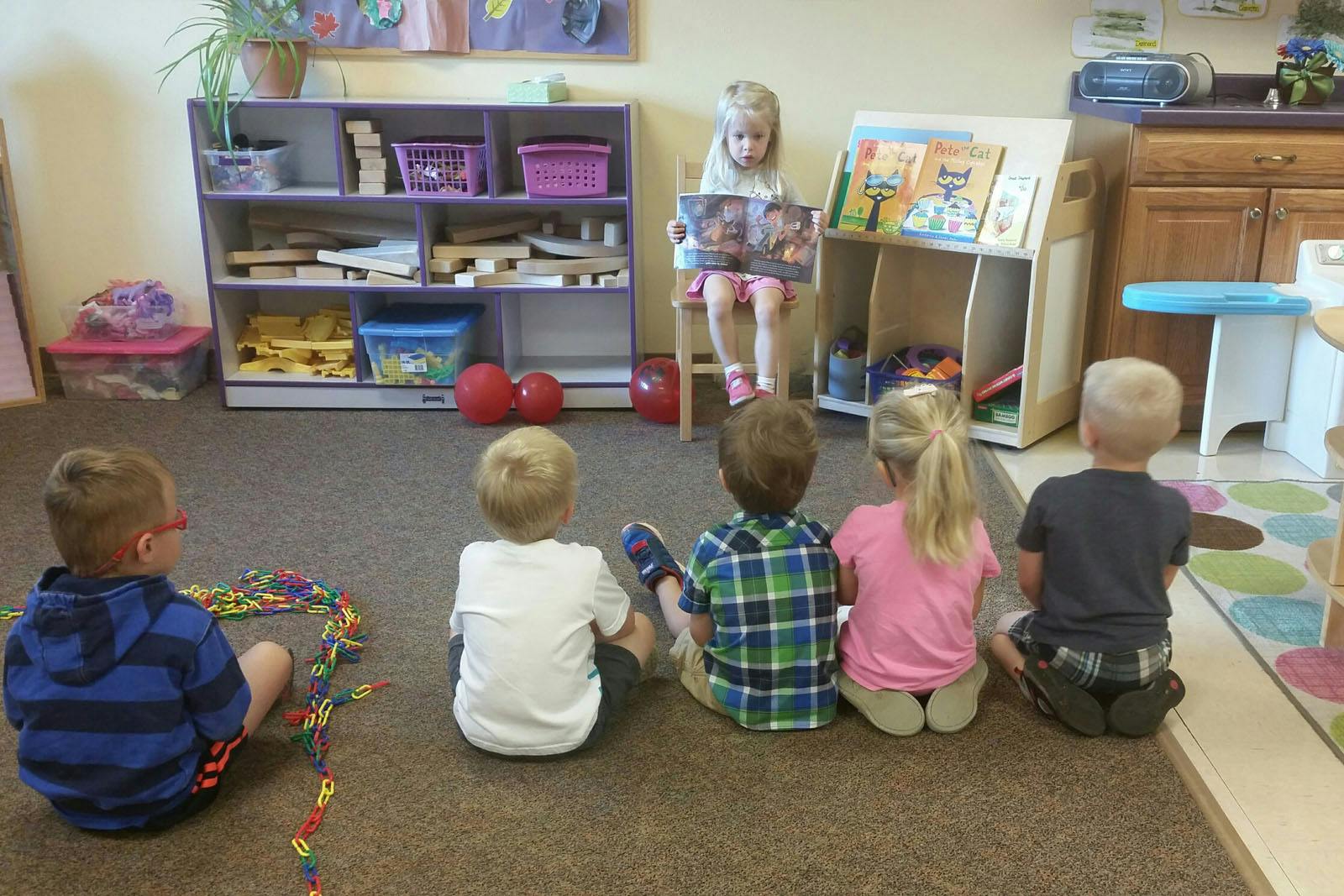 Child reading a book to four children sitting on the floor in a classroom