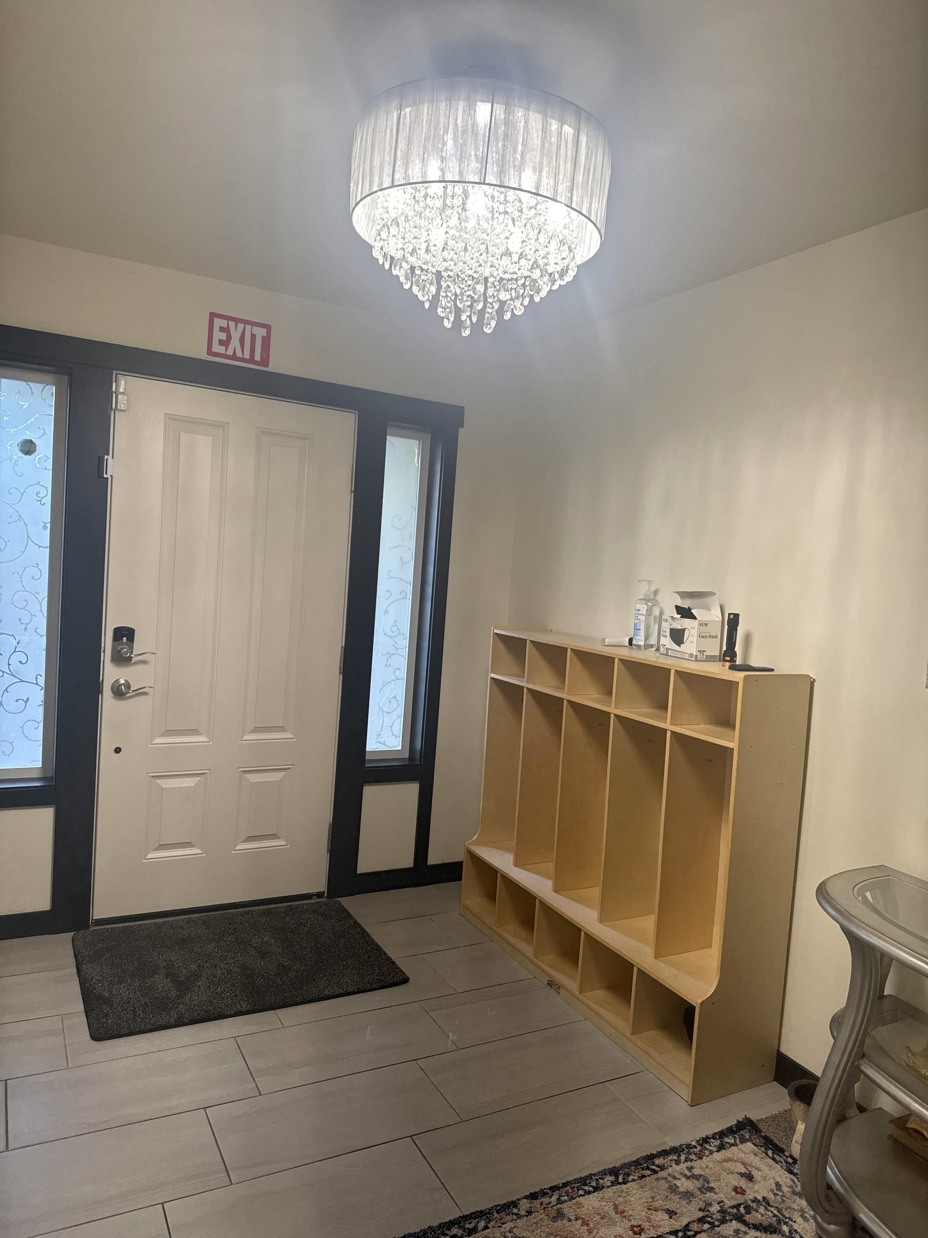 Entryway with a white door, an "EXIT" sign, and a wooden cubby shelf