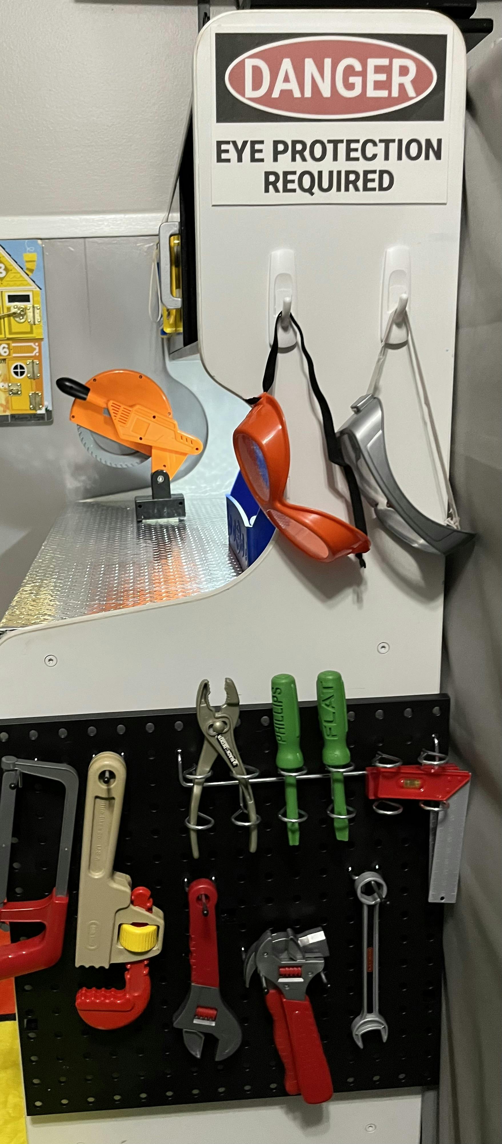 Danger sign with eye protection required, safety glasses, and tools on a pegboard