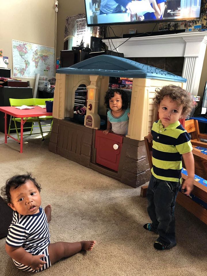 Three children playing, one in a playhouse, one standing, and one sitting on the floor