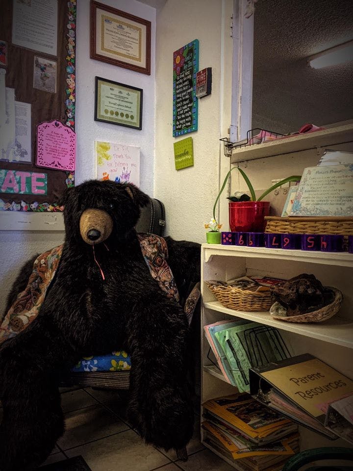 Large stuffed bear sitting in a chair next to a bookshelf