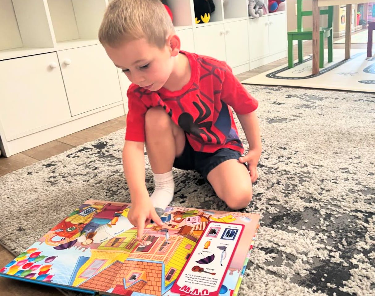 Child kneeling on a rug, pointing at an open book