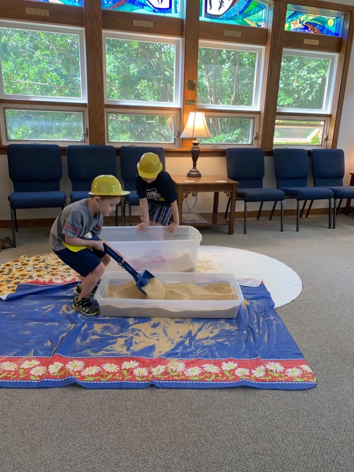 Two children in yellow hard hats playing with sand in plastic bins