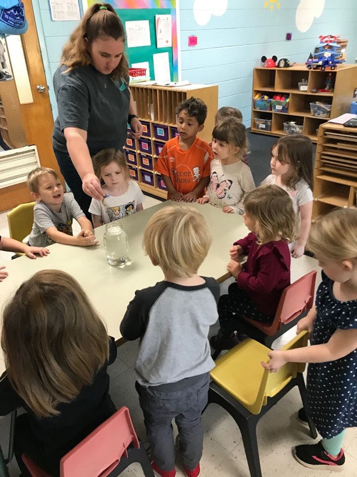 Adult and children gathered around a table in a classroom
