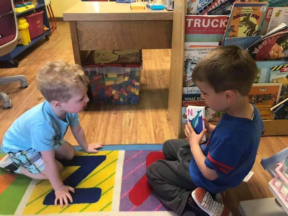 Two children on a rug with letters, one holding a small book