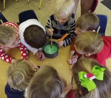 Children gathered around a table, one stirring a green mixture in a pot
