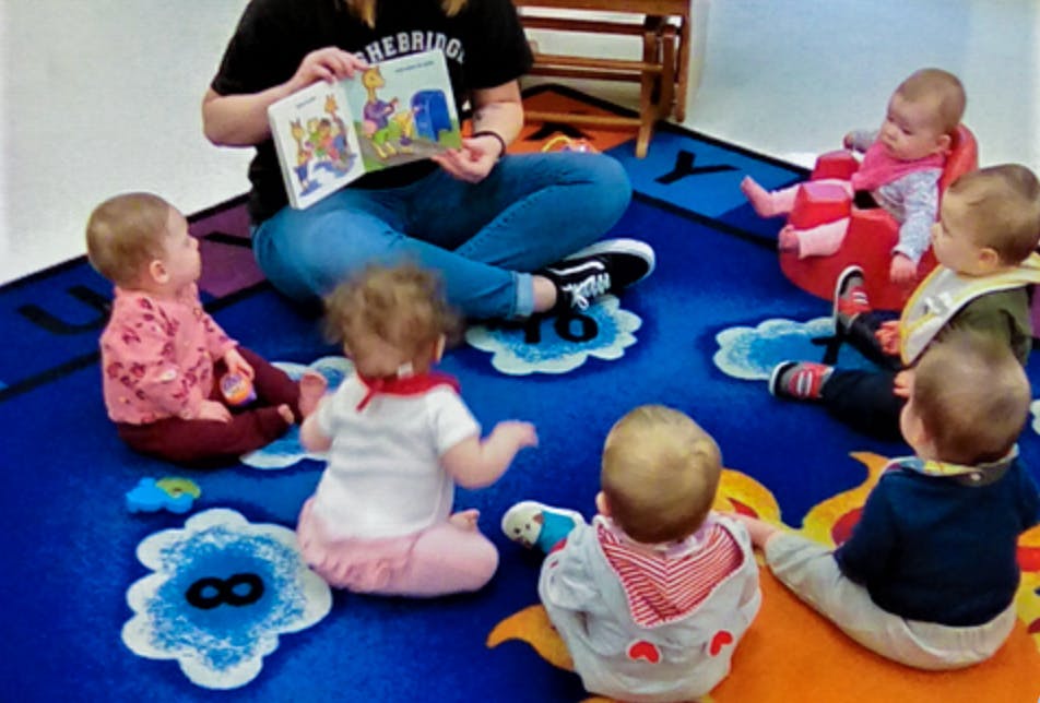 Person reading a book to a group of babies sitting on a rug
