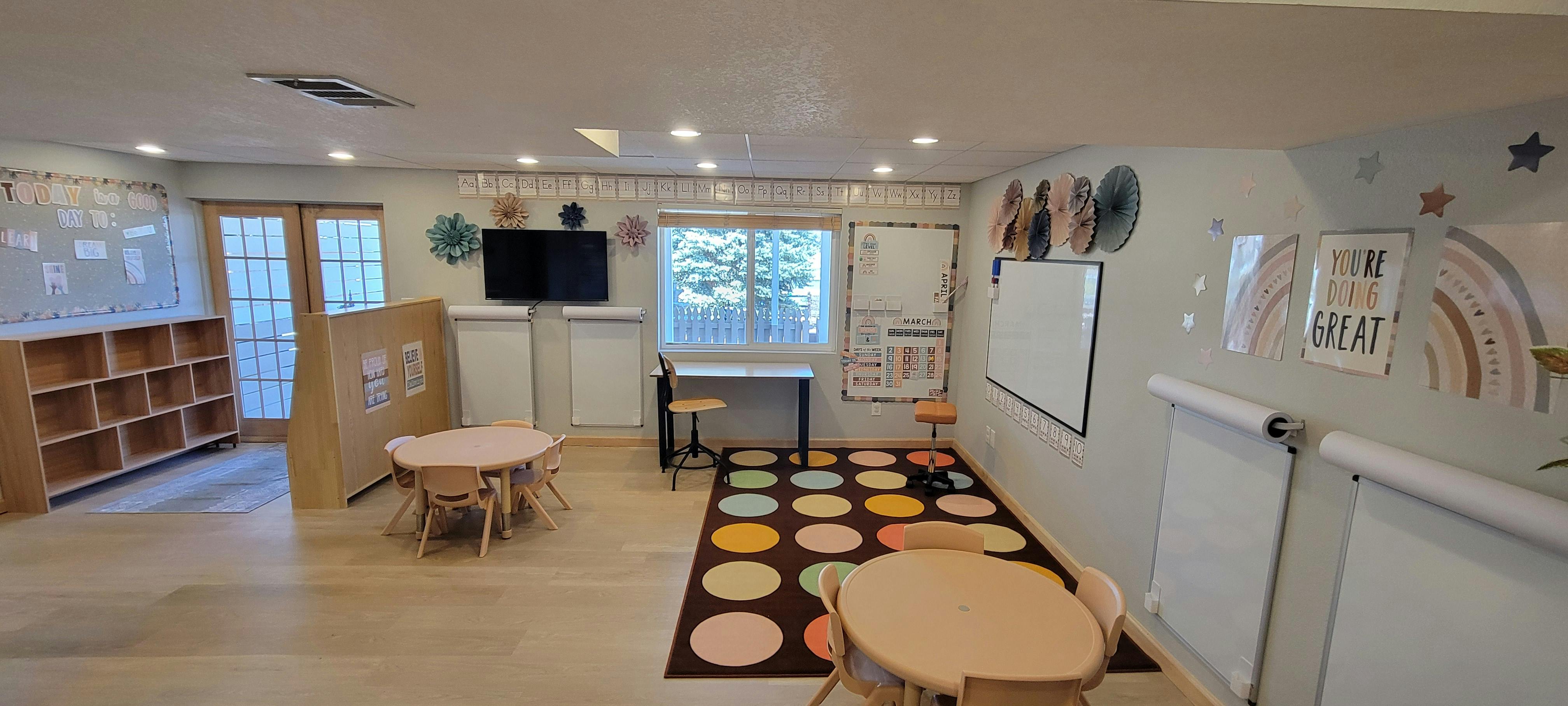 Empty classroom with small tables, chairs, and a colorful rug