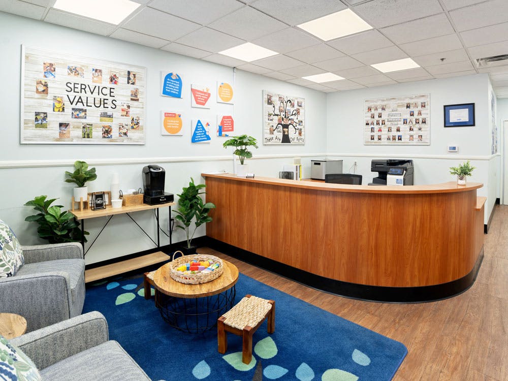 Reception area with a wooden desk, coffee station, armchairs, and wall art