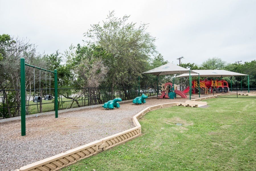 Playground with swings, spring riders, and play structure under shade canopies