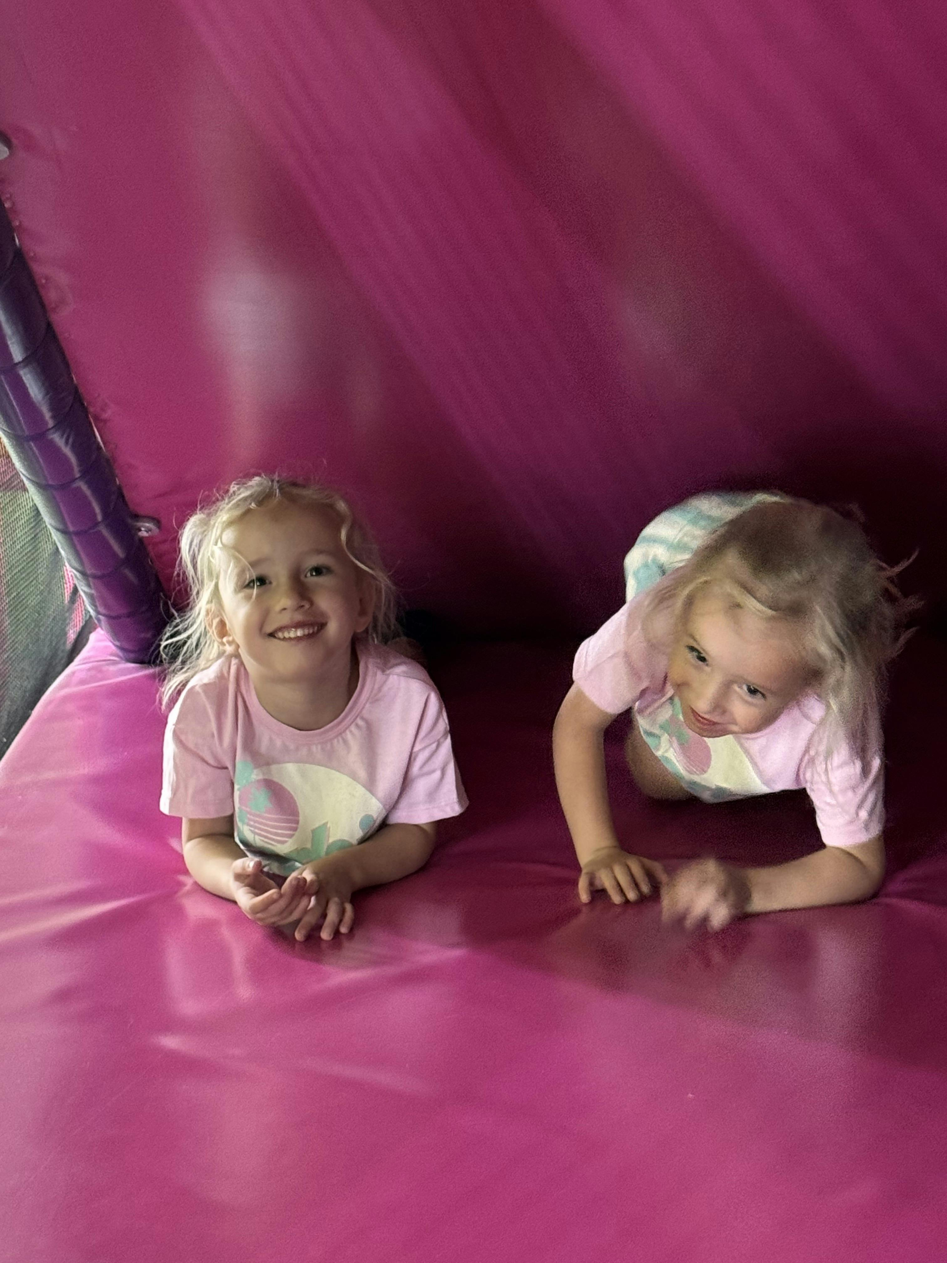 Two children on a pink surface, one smiling and one crawling