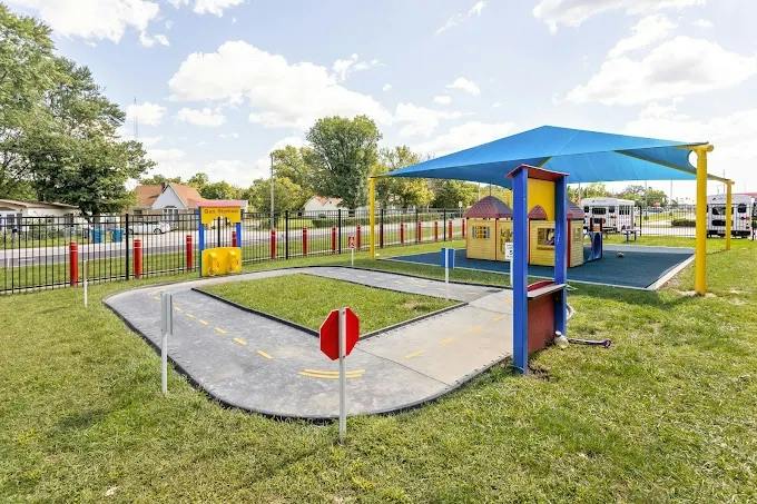 Outdoor playground with miniature roads, stop sign, gas station, and playhouses