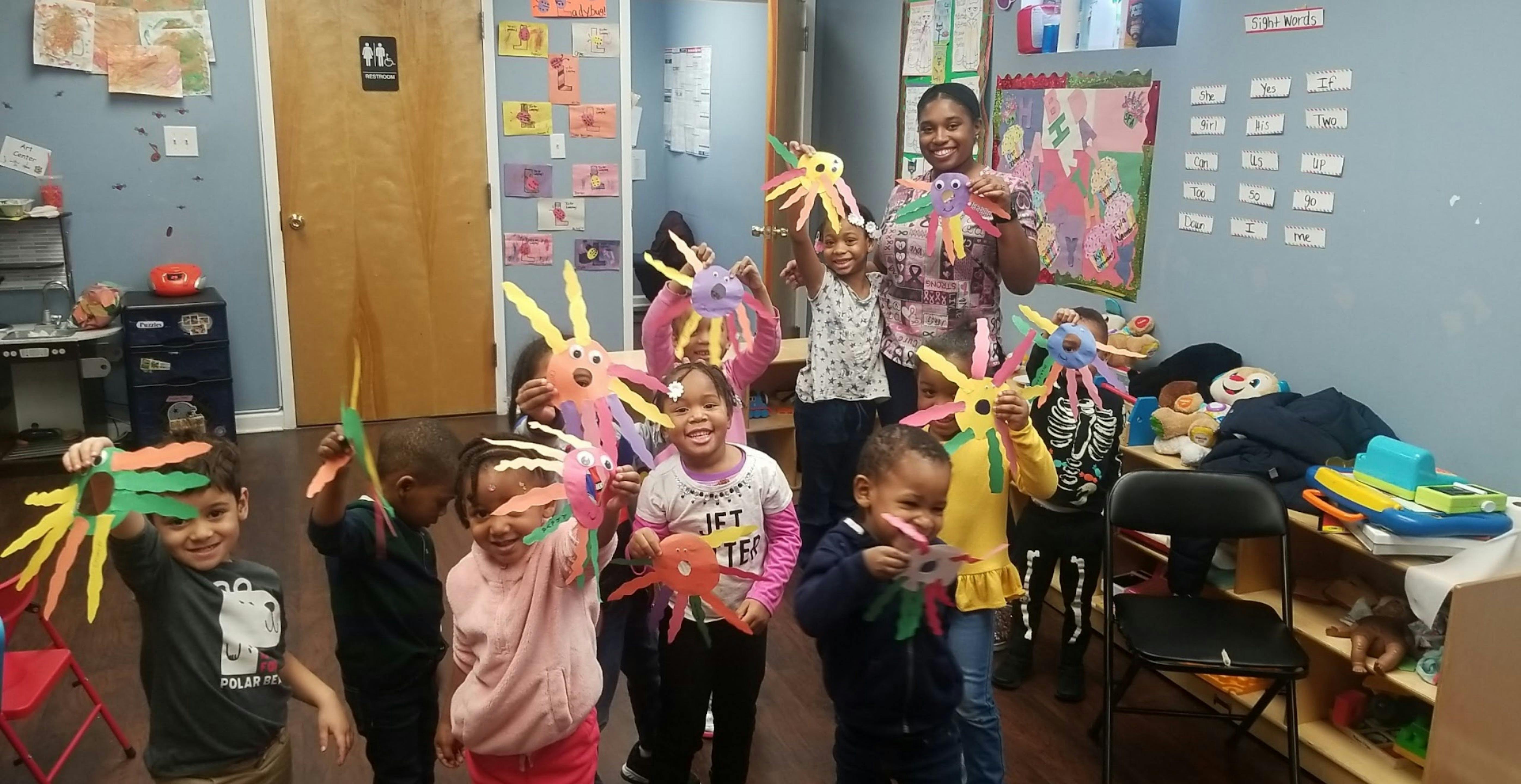 Adult and children holding up colorful crafts in a classroom
