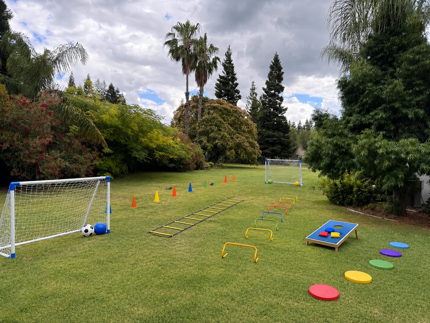 Outdoor lawn with soccer goals, agility ladder, mini hurdles, and cornhole game