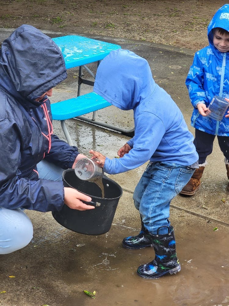 Person and child in hooded jackets pouring liquid into a bucket
