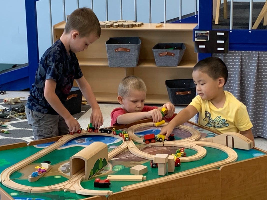 Three children playing with a wooden train set on a table