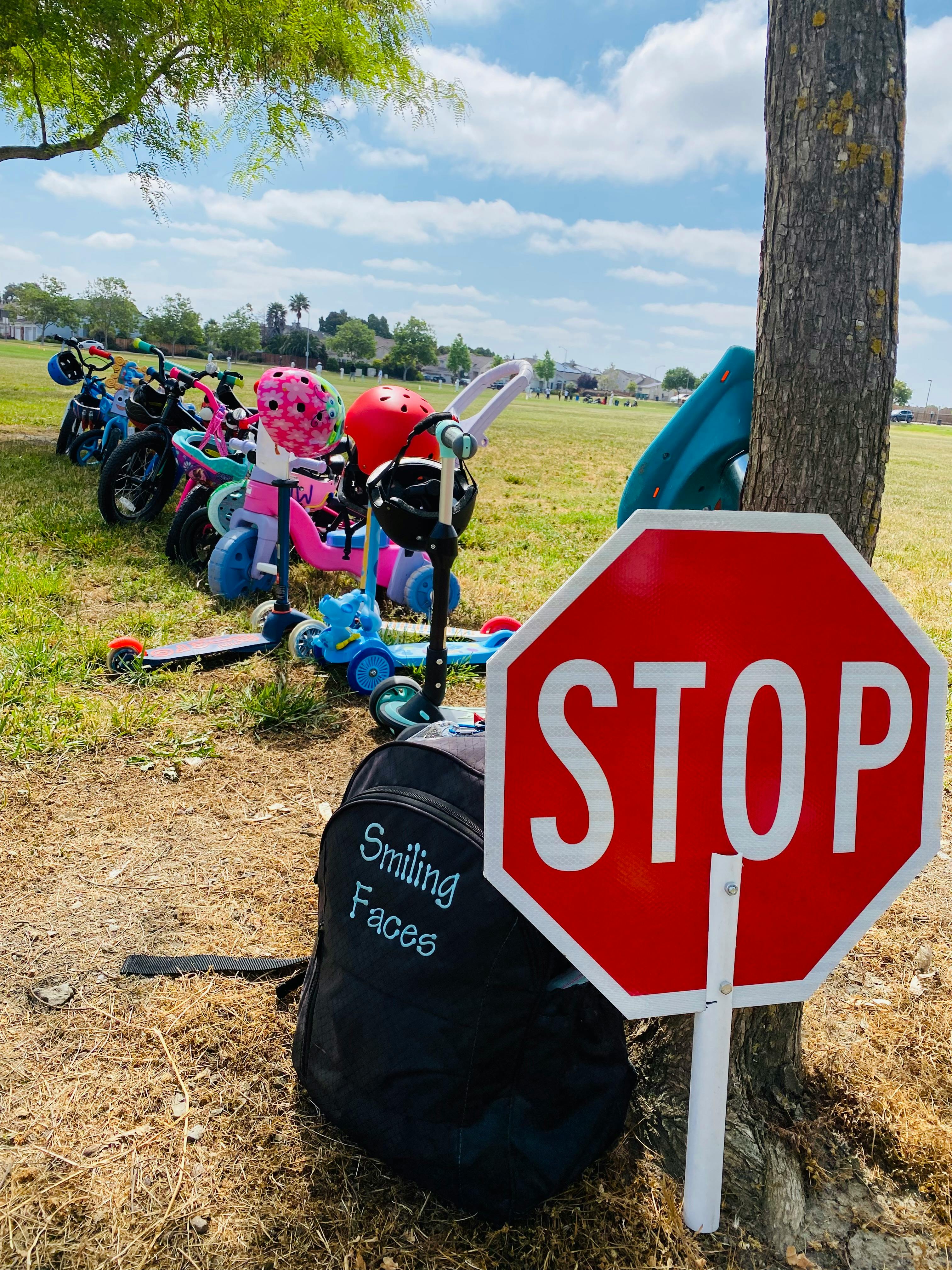Stop sign next to a tree with children's bikes and scooters in the background