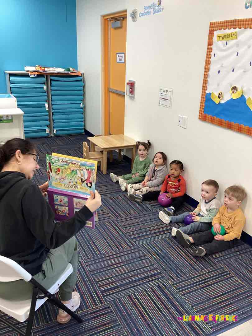 Person reading to multiple children sitting on the floor in a classroom