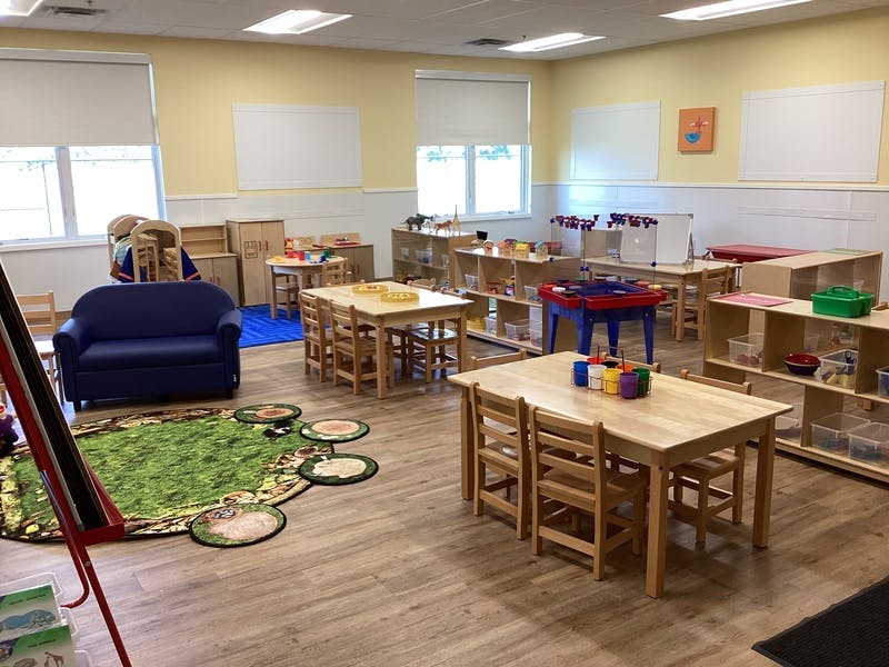 A colorful classroom with tables, chairs, a blue couch, and a green rug