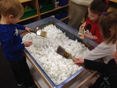 Children playing with brushes in a bin of white packing peanuts