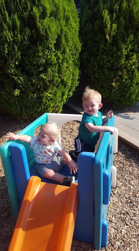 Two children playing on a small plastic slide and play structure