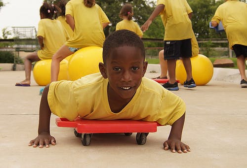 Child on a red scooter board with other children in background
