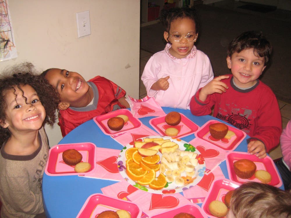 Four children sitting around a table with fruit and cupcakes