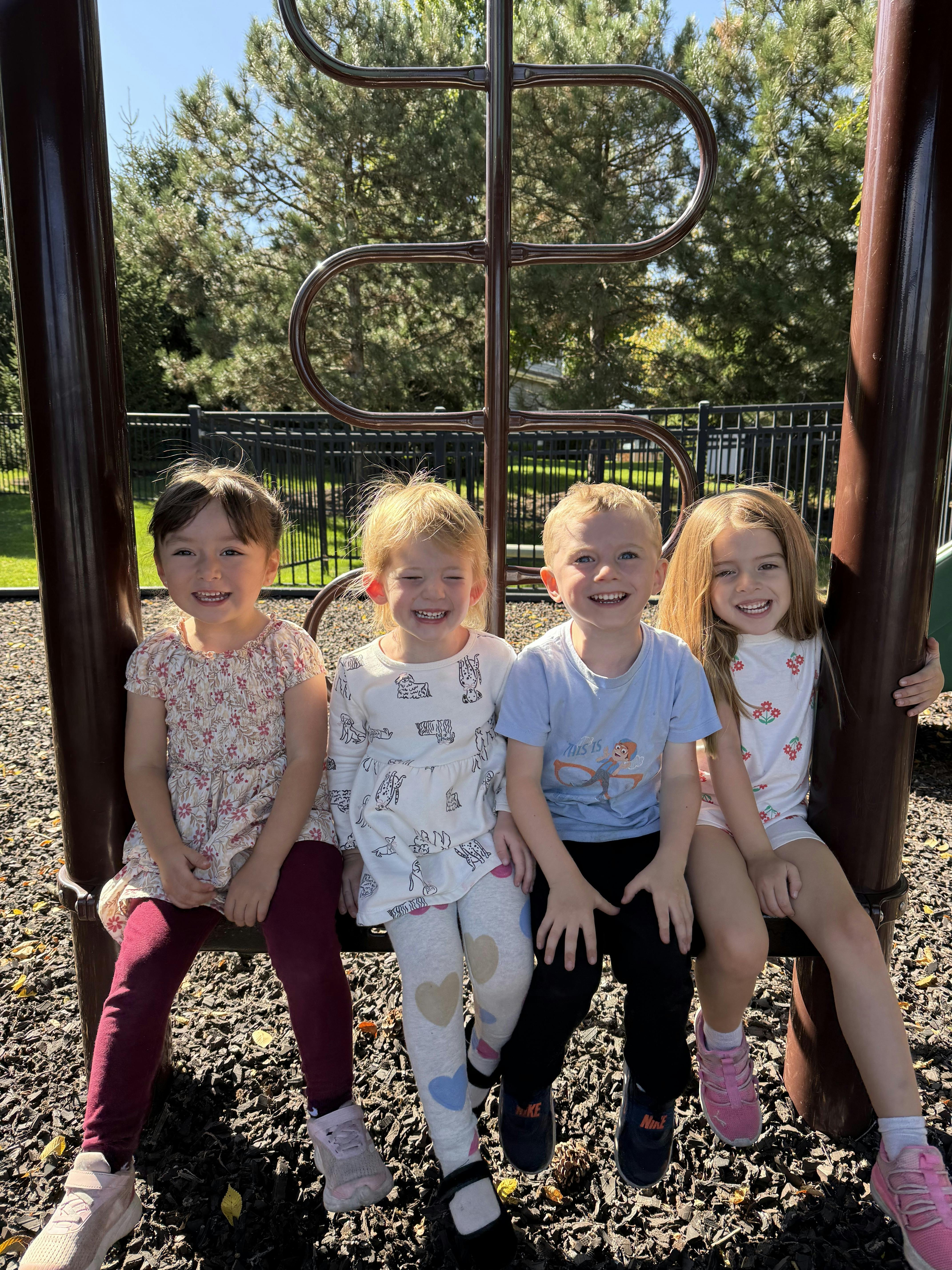 Four children sitting together on playground equipment