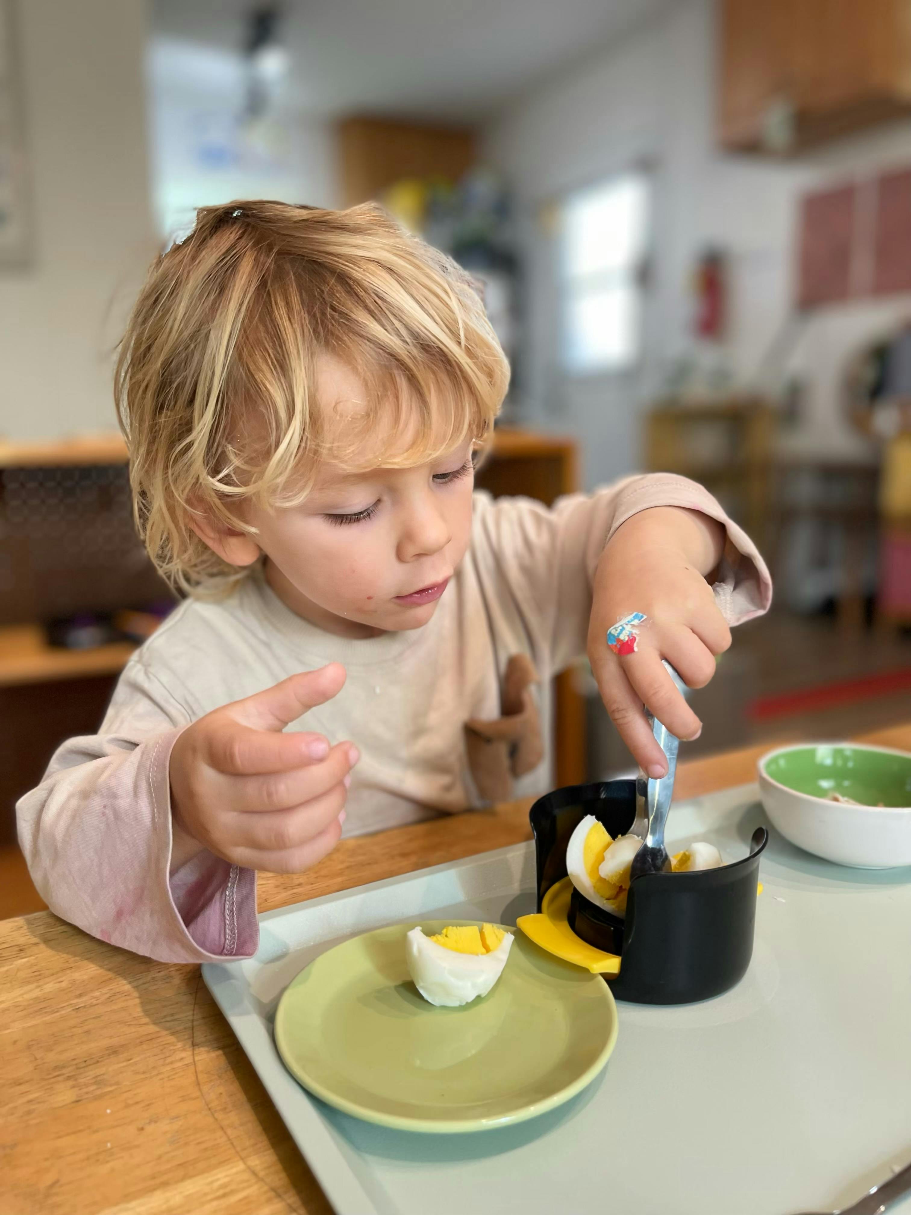 Child cutting a hard-boiled egg with a utensil