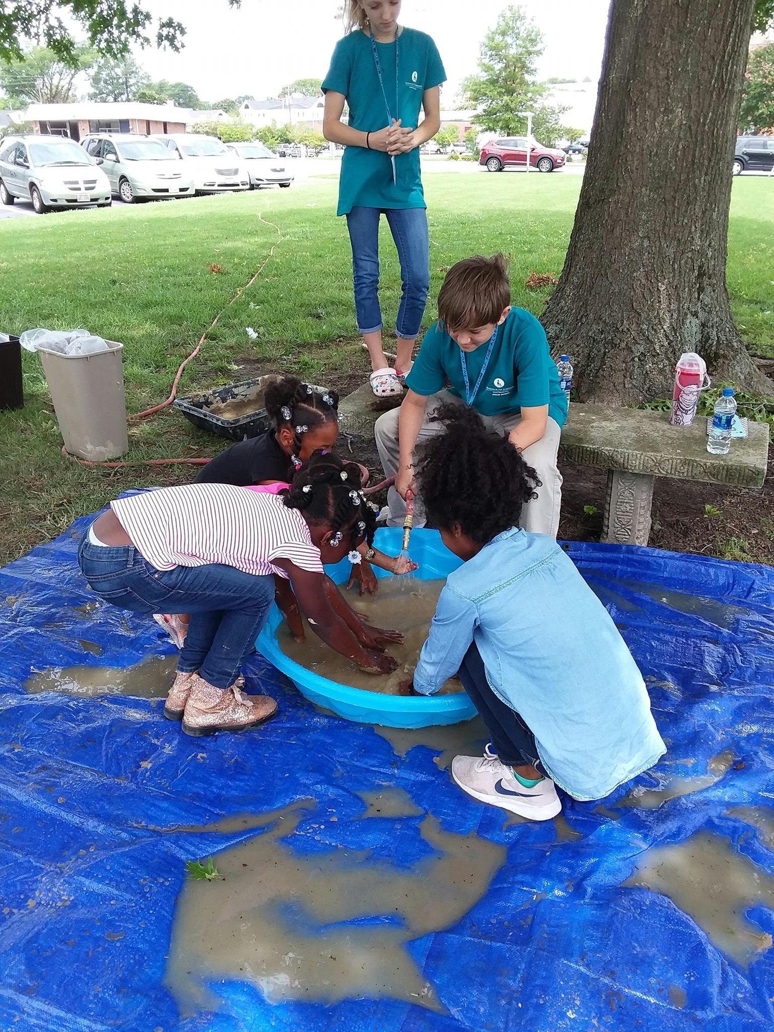 Children playing in a blue basin filled with mud and water on a tarp