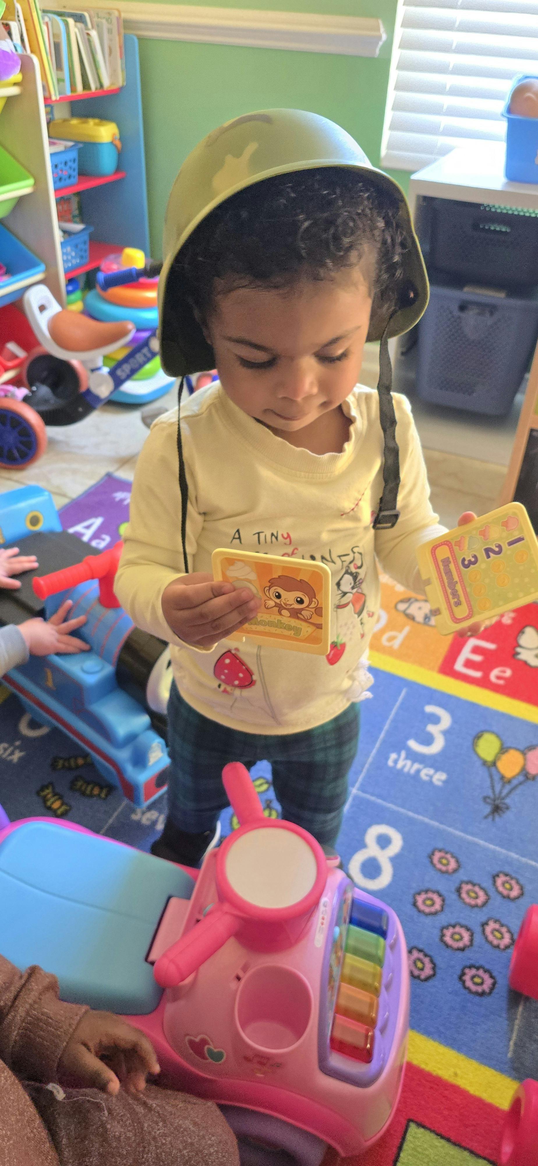 Child wearing a helmet, holding learning cards with monkey and numbers
