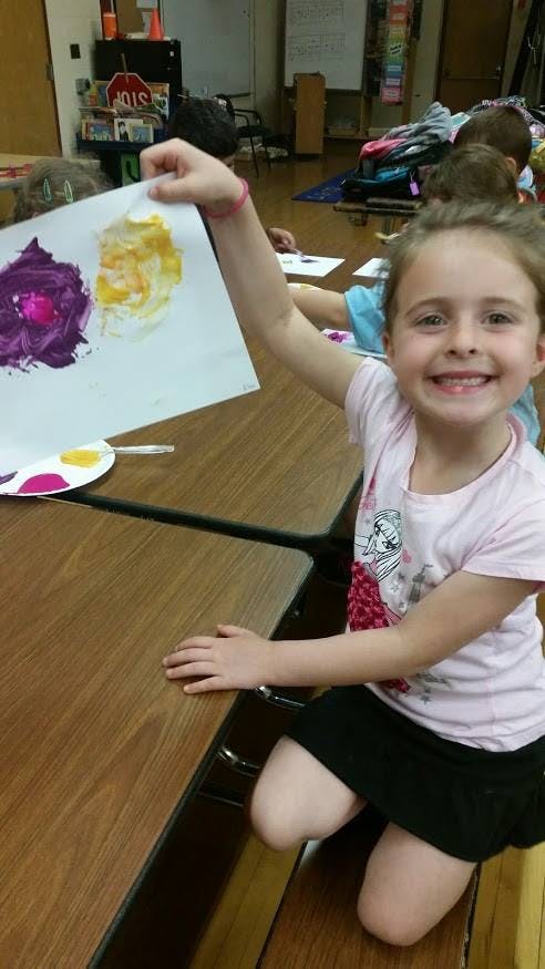 Child holding up a paper with purple and yellow paint on it