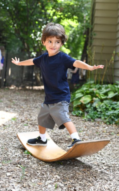 Child balancing on a wooden wobble board outdoors
