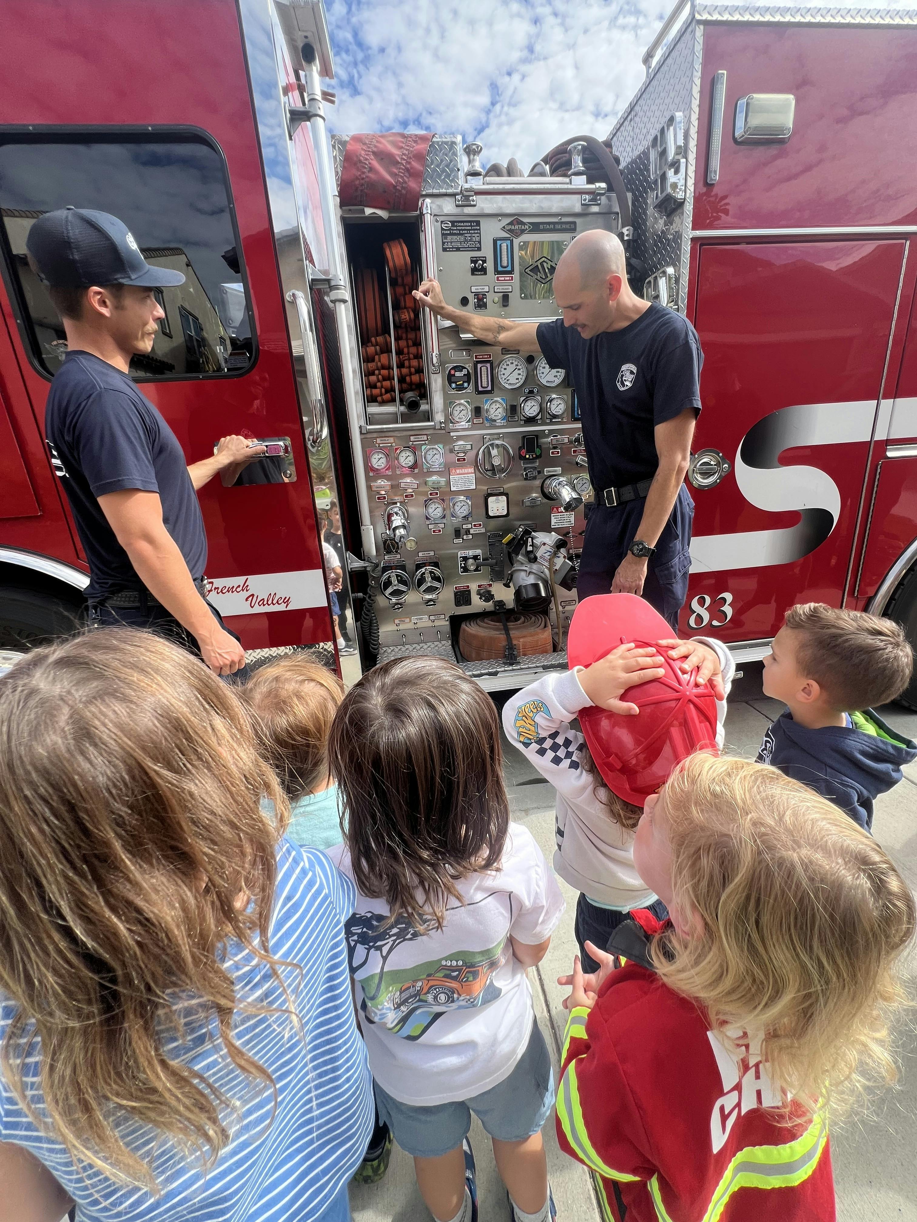 Two people showing children the controls on a fire truck
