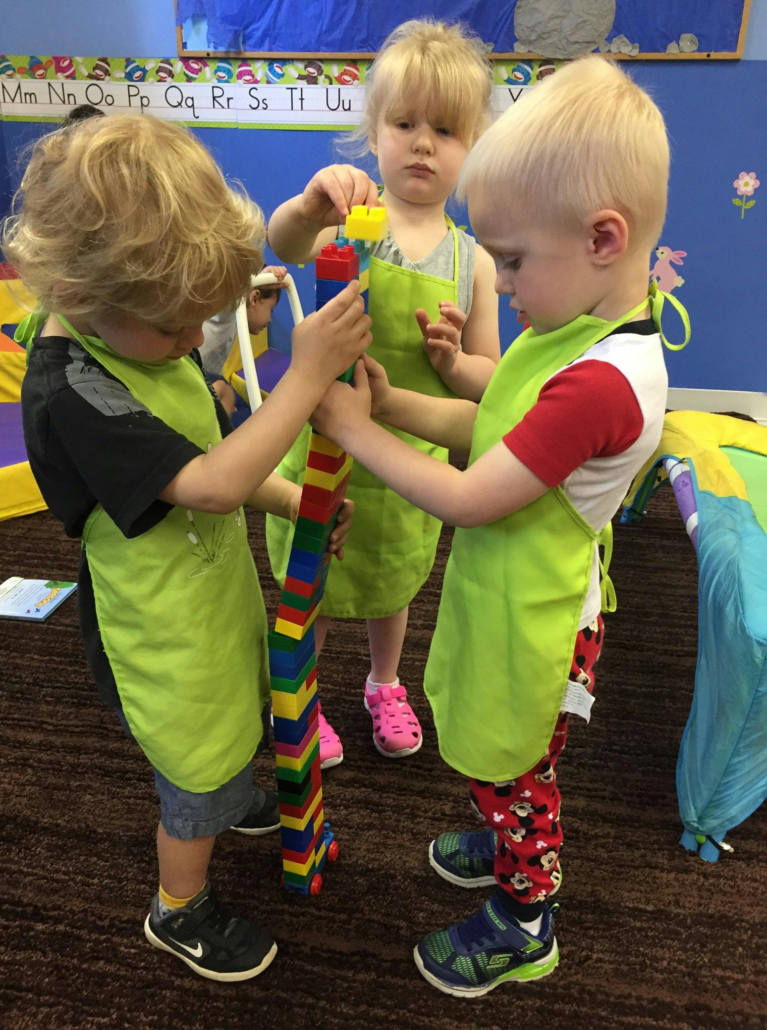 Three children in aprons building a tall tower with colorful blocks