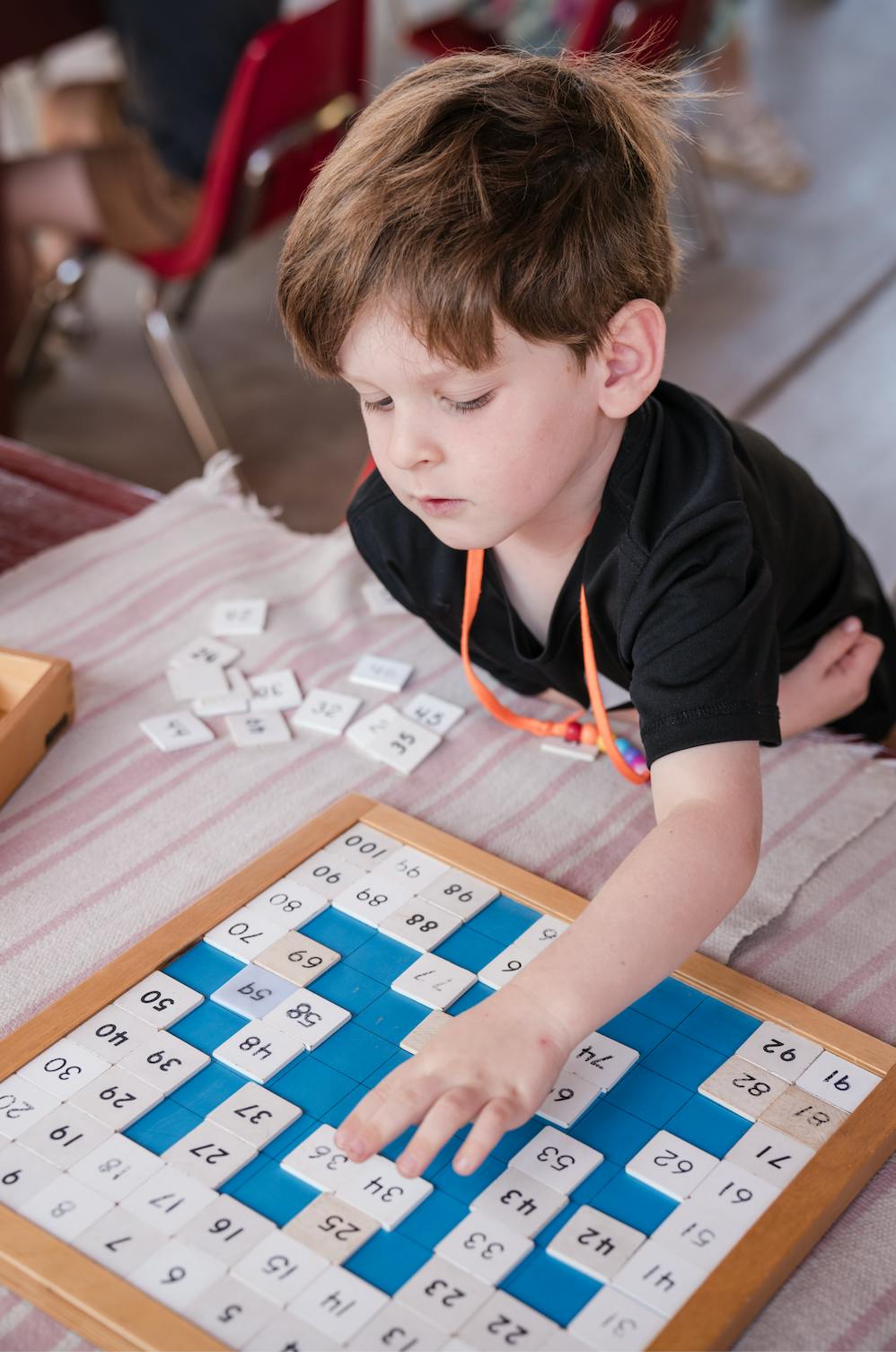 Child placing a numbered tile onto a board containing numbers one through 100