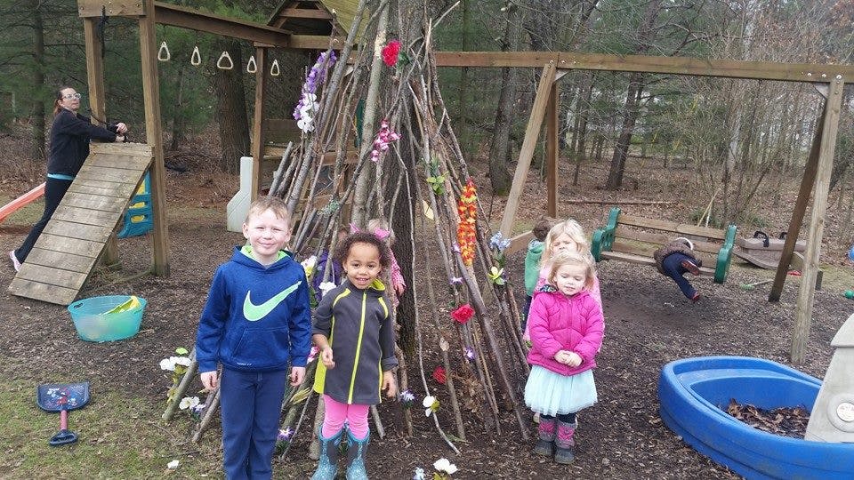 Children standing in front of a stick teepee on a playground