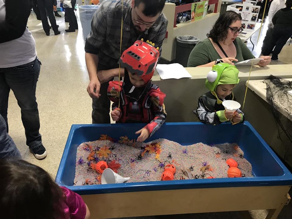 Adult and two children playing in a sensory bin with sand and toys