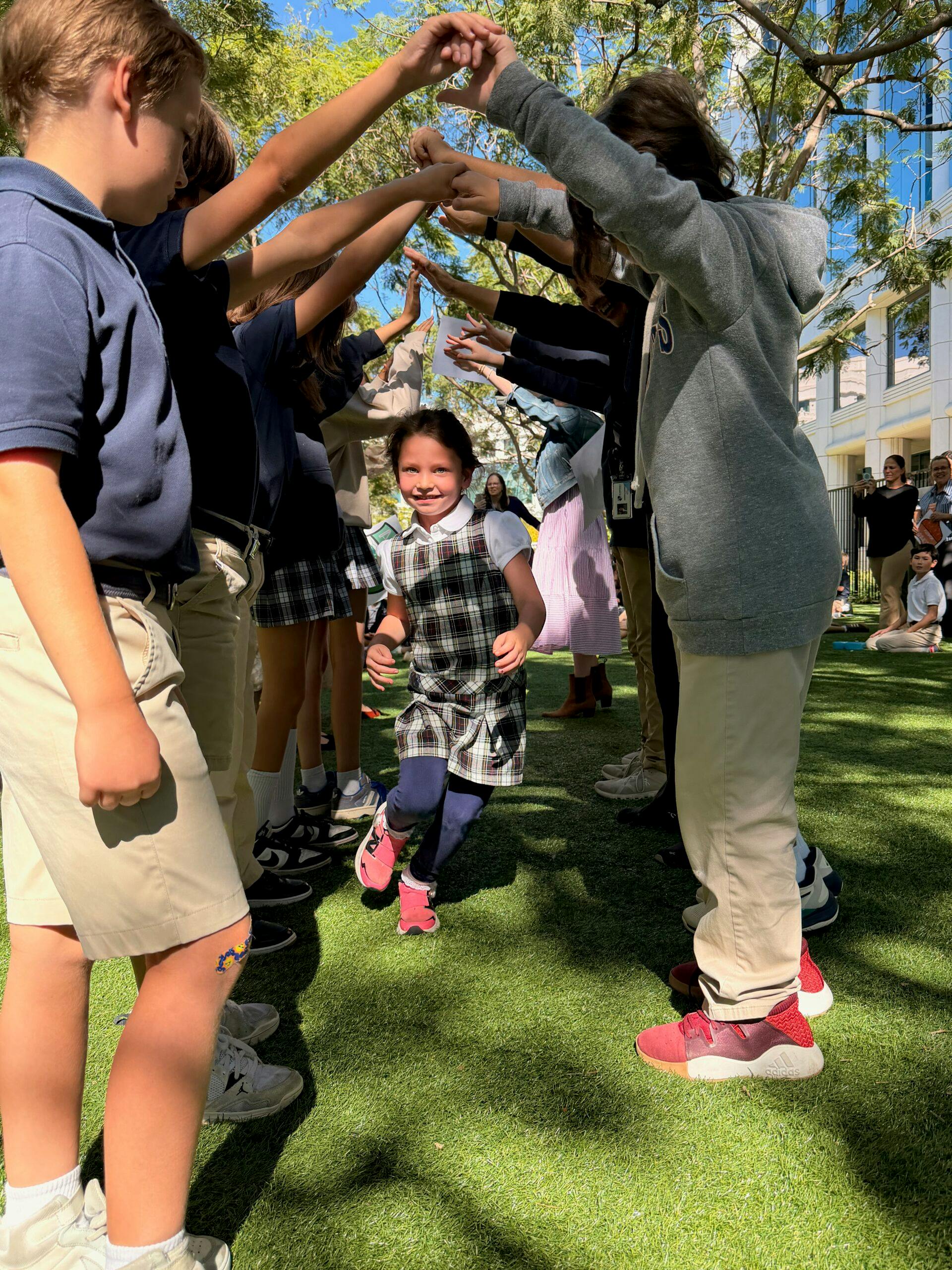 Child running through an arch formed by many arms of older children