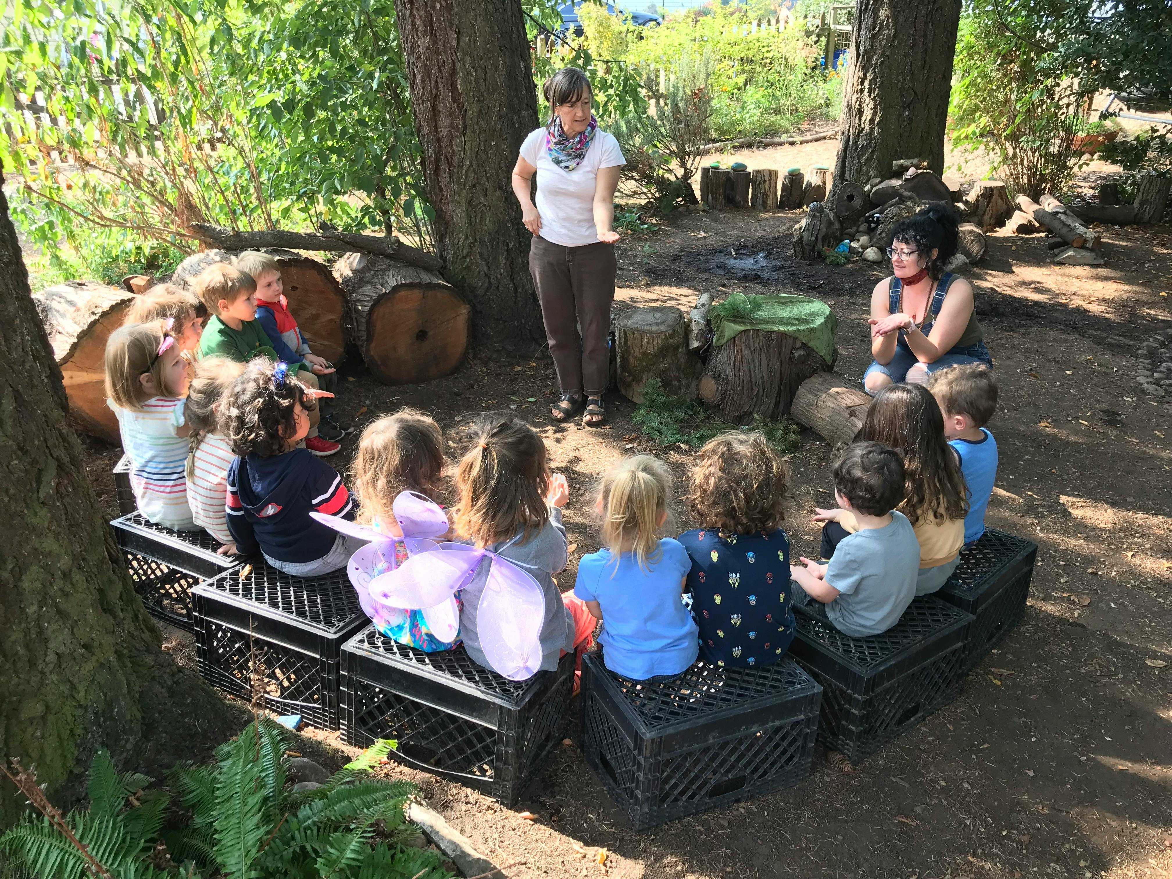 Two people with a group of children sitting in a circle outdoors