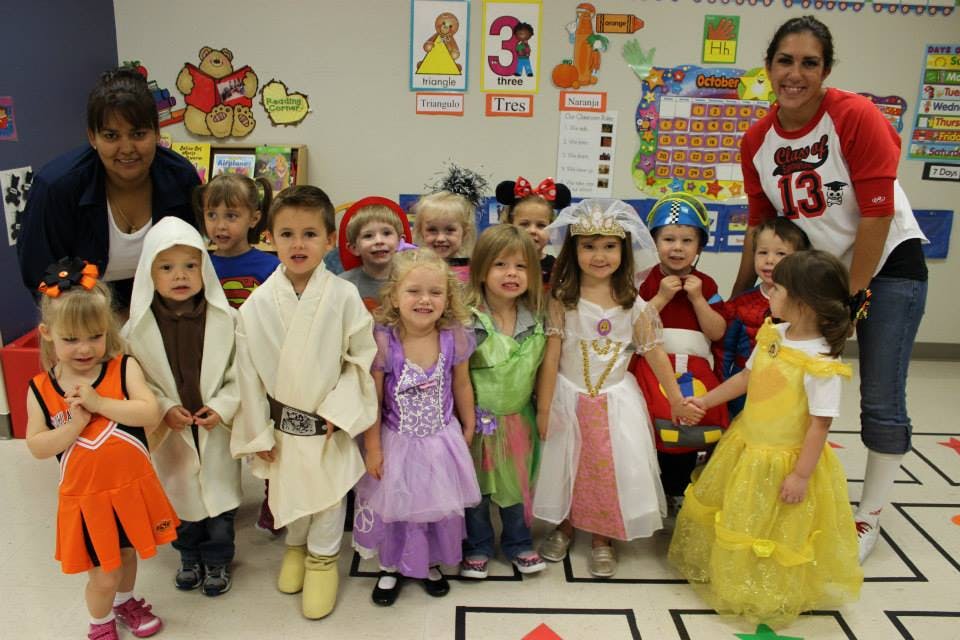 Two adults with a group of children in costumes in a classroom