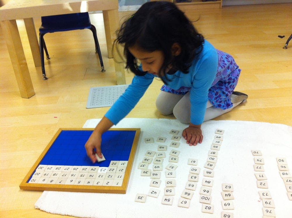 Child kneeling and placing a numbered tile onto a blue board