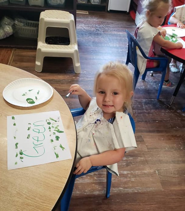 Child painting a picture with the word "Green" on it