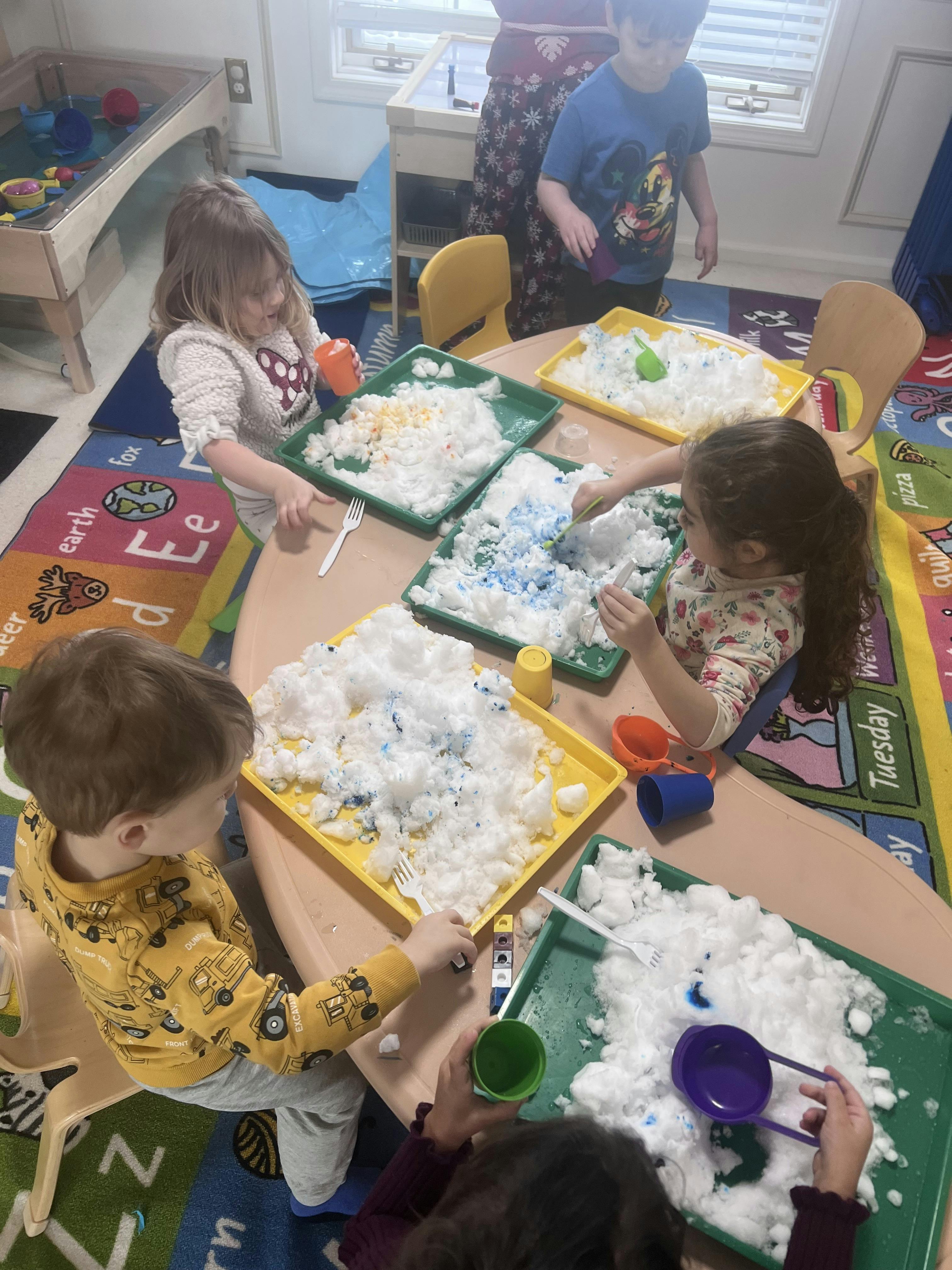Children playing with white sensory bins containing colorful snow-like material