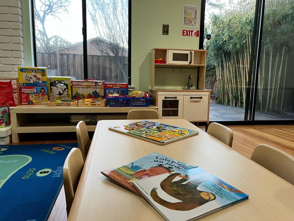 Children's books on a table in a classroom with a play kitchen and toys