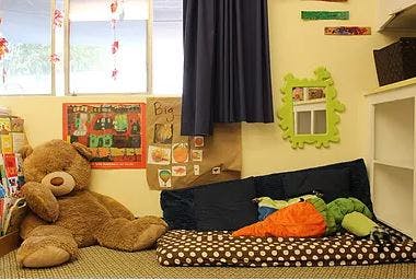 Large teddy bear next to a beanbag chair and floor cushion with stuffed toys